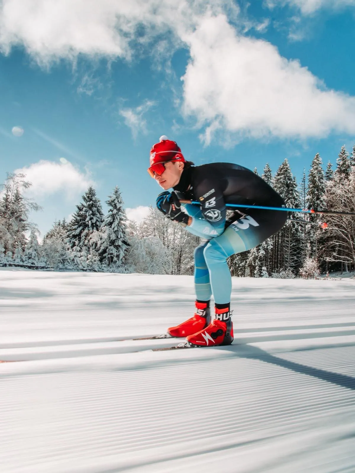 Noa Genest, bonnet rouge, file en position de recherche de vitesse sur une piste damée, sous un grand ciel bleu