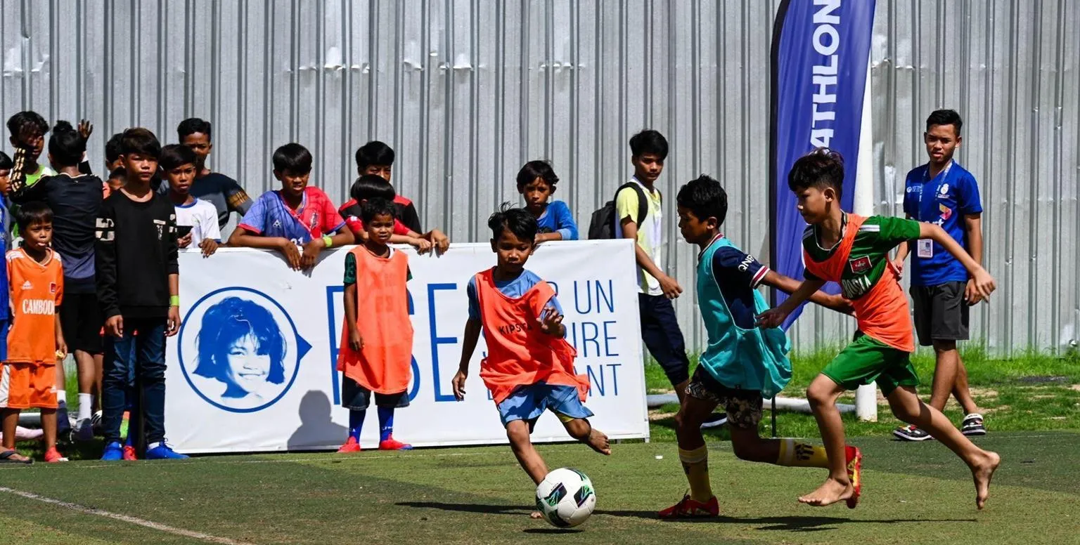 De jeunes Cambodgiens disputent un match de football devant une banderole Pour un Sourire d'Enfant