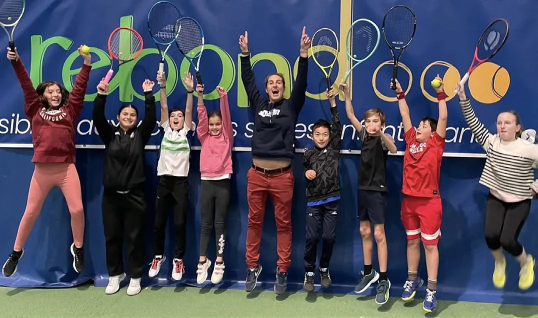 De jeunes joueurs de tennis sautent de joie, raquettes levées, devant une banderole Rebond