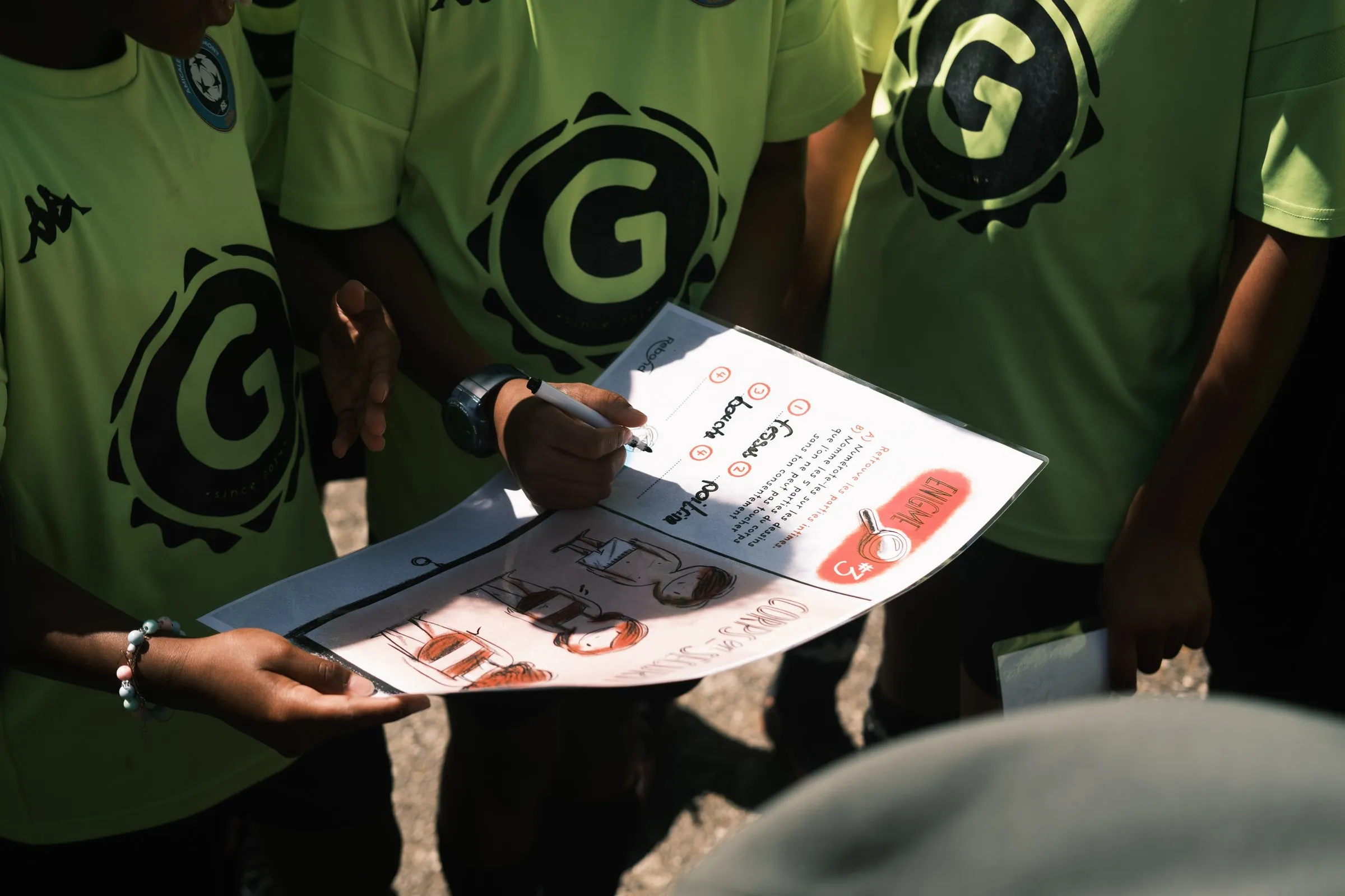 De jeunes footballeurs en maillot vert remplissent une fiche « Énigme » de Rebond sur le respect du corps