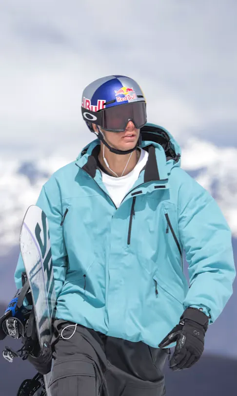 Romain Allemand, casque et masque sur la tête, snowboard sous le bras face aux montagnes enneigées